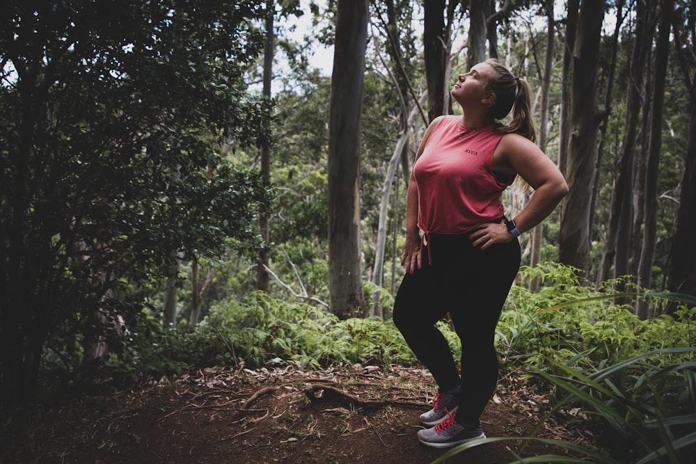 mulher na regata vermelha e calças pretas em pé na floresta durante o dia