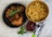 A black skillet contains four pieces of roasted chicken adorned with a sprig of fresh rosemary, while a brown bowl holds a generous serving of golden french fries. A small glass dish filled with ketchup is positioned beside silverware, all set on a green-striped fabric.