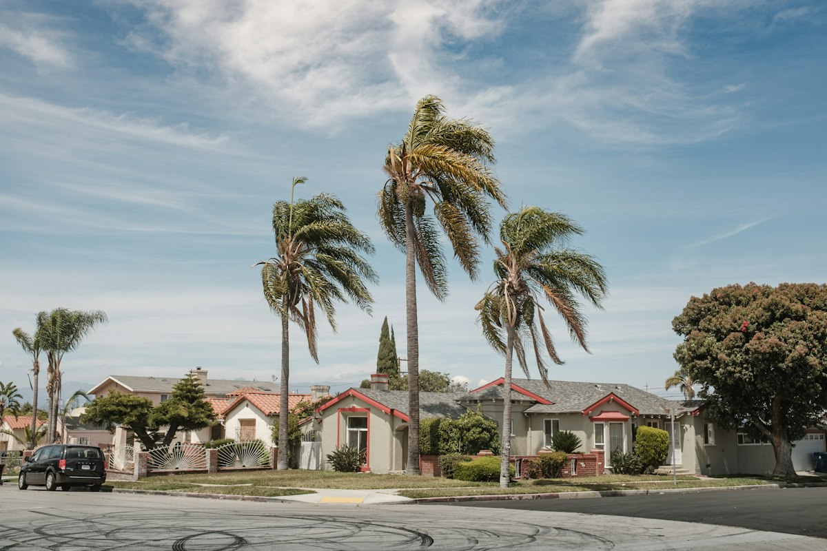 A white house with red accents near palm trees under a blue sky