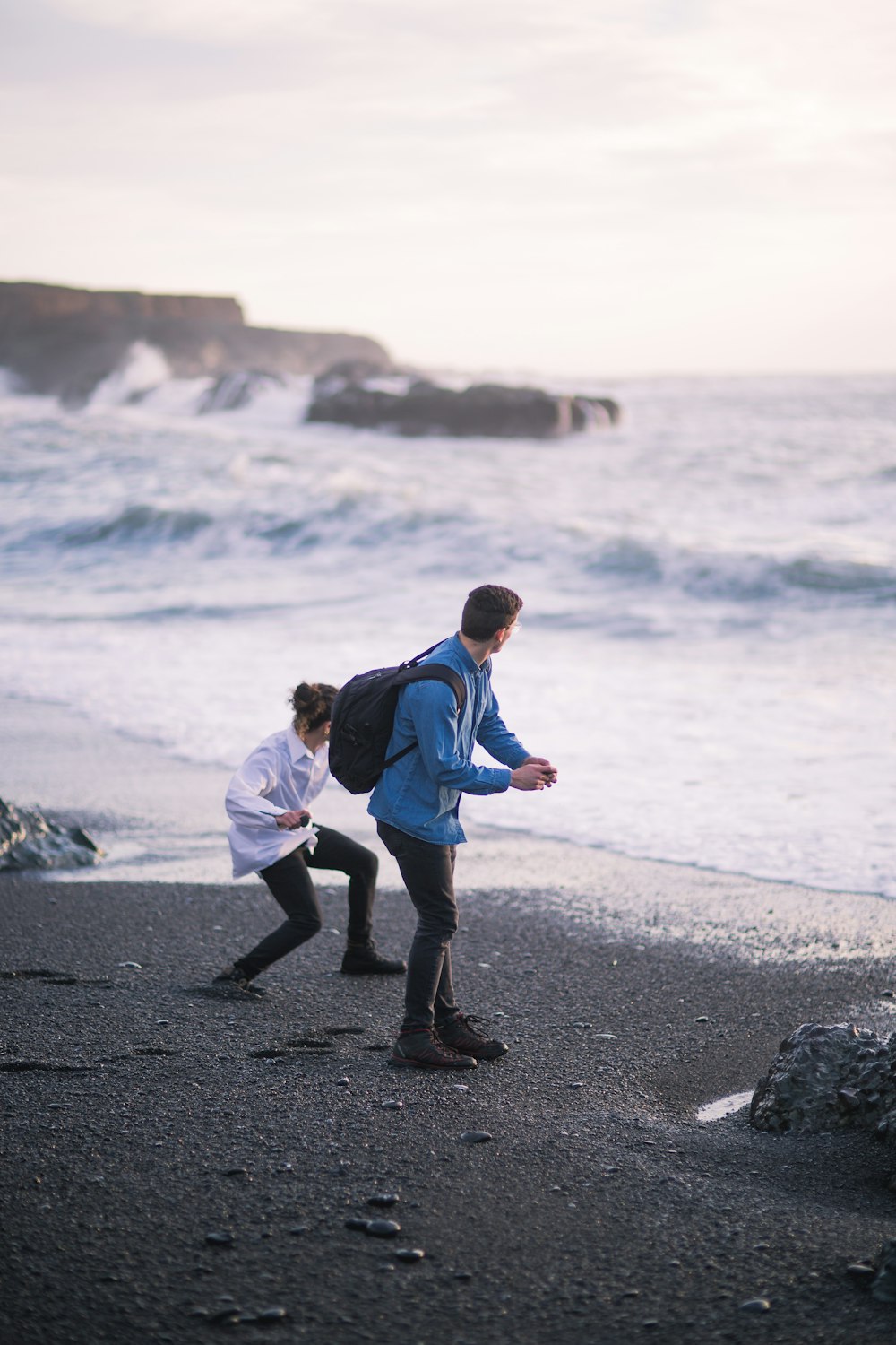 파란색 재킷과 검은 바지를 입은 남자가 낮 동안 해변을 걷고 있다