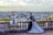 Two individuals dressed in bold, avant-garde fashion pose on a stone balustrade overlooking a panoramic cityscape. The outfits feature striking black and white stripes with elements of modern design, set against a background of a sprawling urban landscape under a cloudy sky.