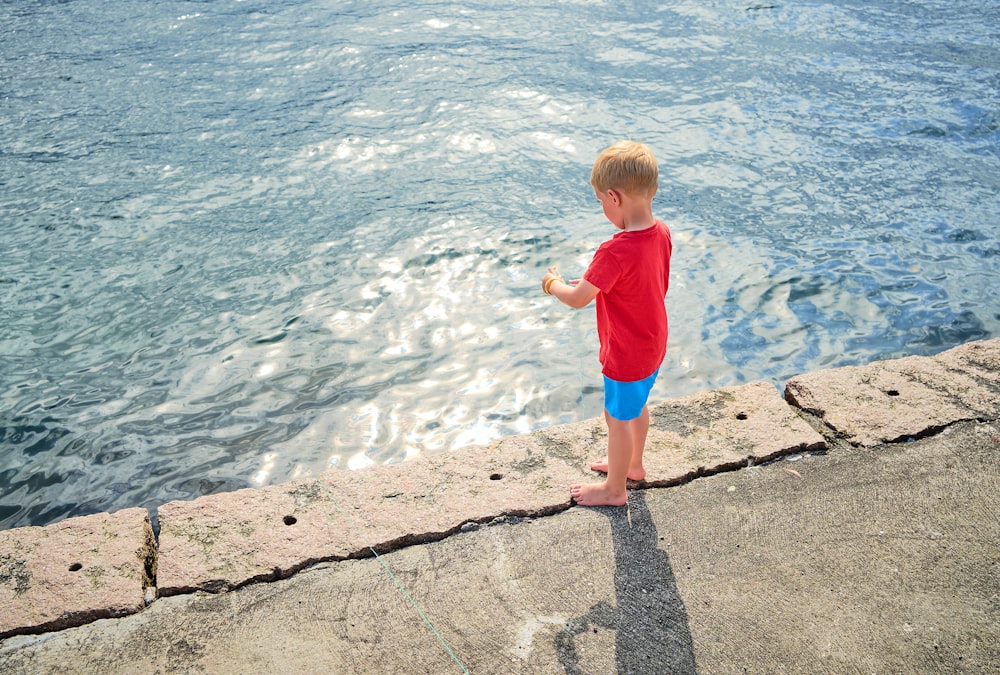 girl in pink shirt standing on gray concrete dock during daytime