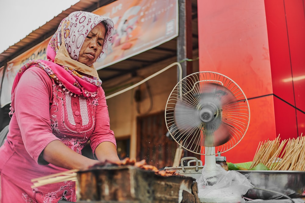 woman in pink and white hijab sitting beside blue desk fan