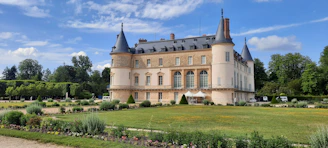 A charming historic castle surrounded by lush gardens under a clear blue sky.