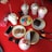 An assortment of colorful desserts and drinks on a bright red table, including various milkshakes topped with whipped cream and chocolate syrup, colorful macarons, cookies, slices of chocolate cake, a smartphone, sunglasses, and a wallet.