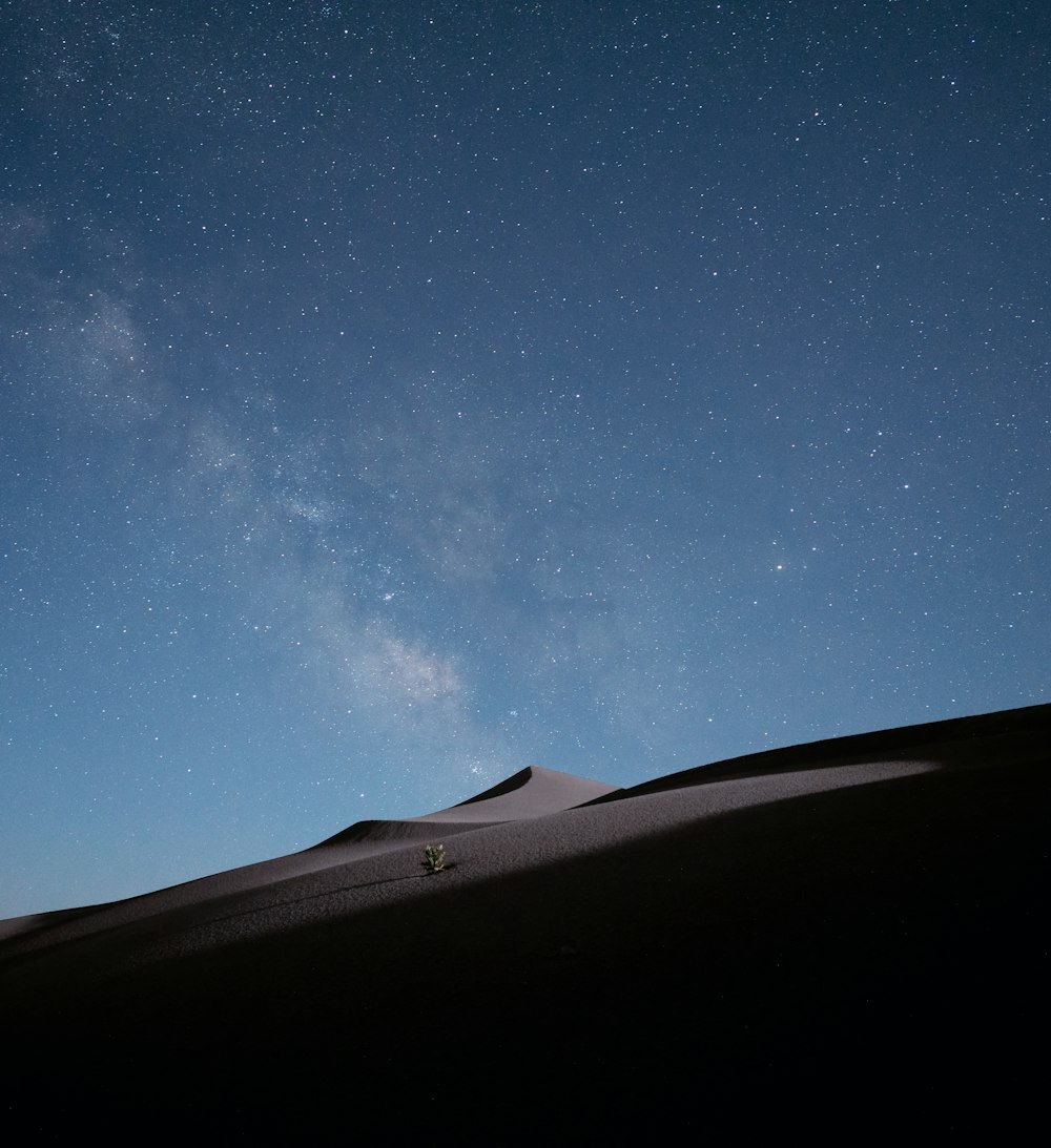 Silueta de la persona de pie sobre la arena marrón bajo el cielo azul durante la noche