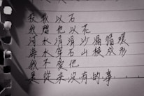 A close-up image of handwritten Chinese characters on lined paper with torn edges. The lighting casts shadows on the paper.