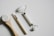 Three beauty tools are arranged on a white surface. A wooden-handled brush with white bristles sits on the left, a white-handled brush with a small, rounded brush head is in the middle, and a white jade roller with metal accents is on the right. The tools appear to be clean and unused.