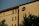 A residential building with a modern architectural design featuring rectangular windows and a distinctive circular window on the upper floor. The facade is illuminated by warm sunlight, casting shadows of nearby trees across the wall.
