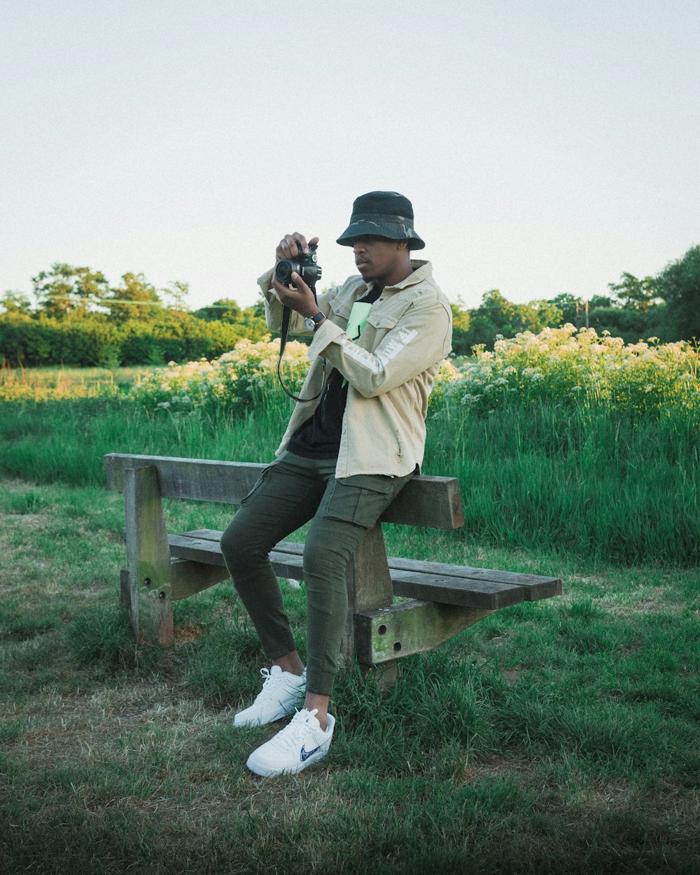 man in beige jacket and blue denim jeans sitting on brown wooden bench during daytime