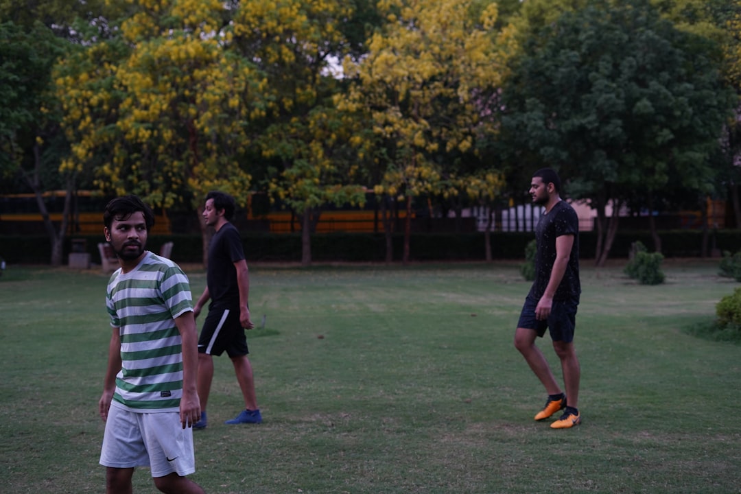 3 men playing soccer on green grass field during daytime