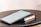 A tablet displaying a document is placed on top of a closed book. Both items rest on a round black table. The document on the tablet screen appears to be text-based, possibly an article or notes.