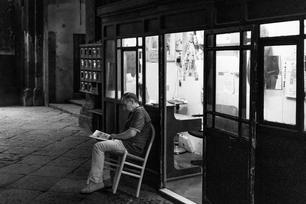 man in black jacket sitting on chair in grayscale photography