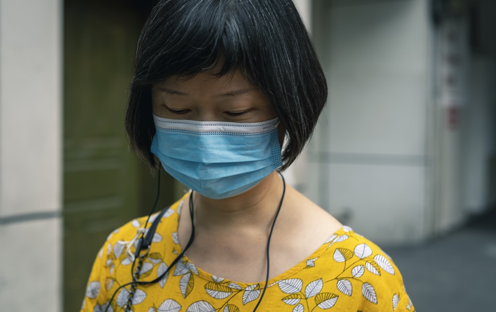 woman in yellow and white floral shirt with blue face mask