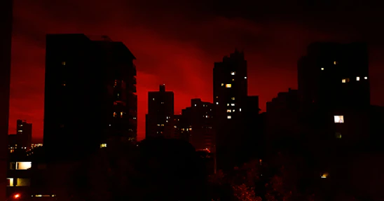 A shadowy city skyline glowing with neon reds and golds under a starry night, hinting at hidden stories within.