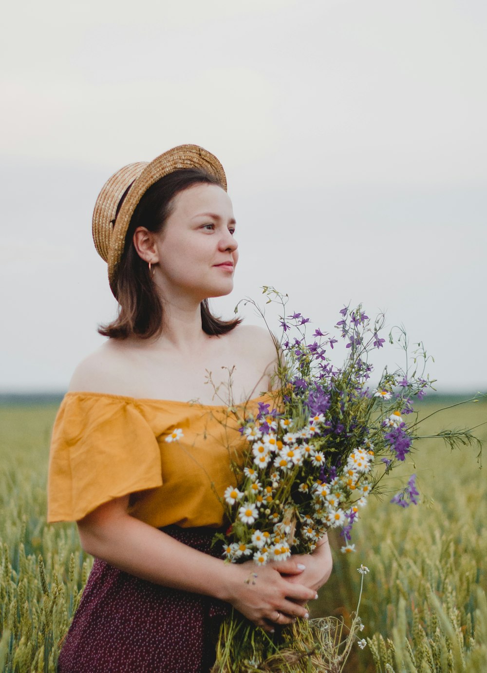 Femme en chemise jaune et chapeau marron tenant des fleurs violettes