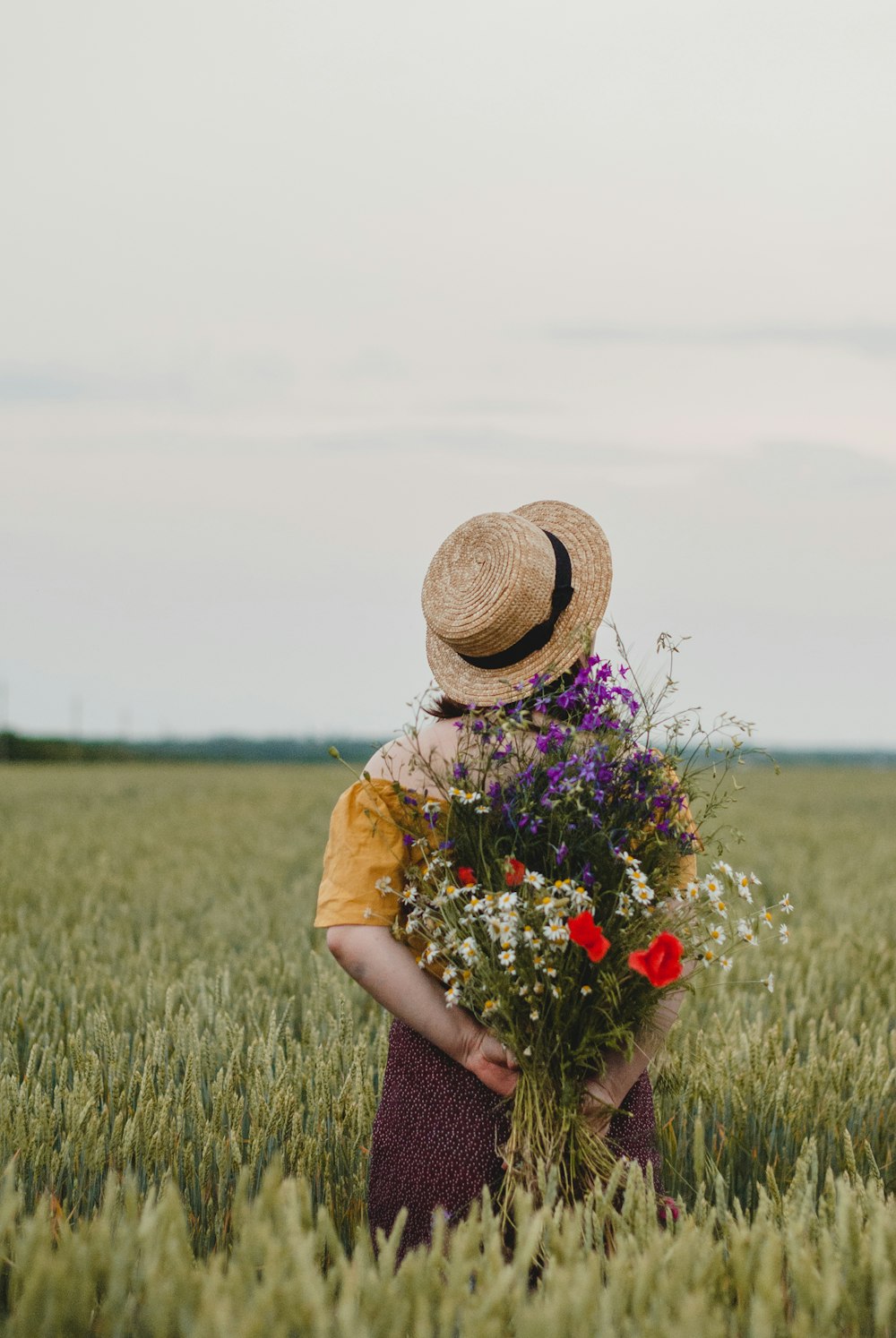 woman in brown sun hat holding red flowers