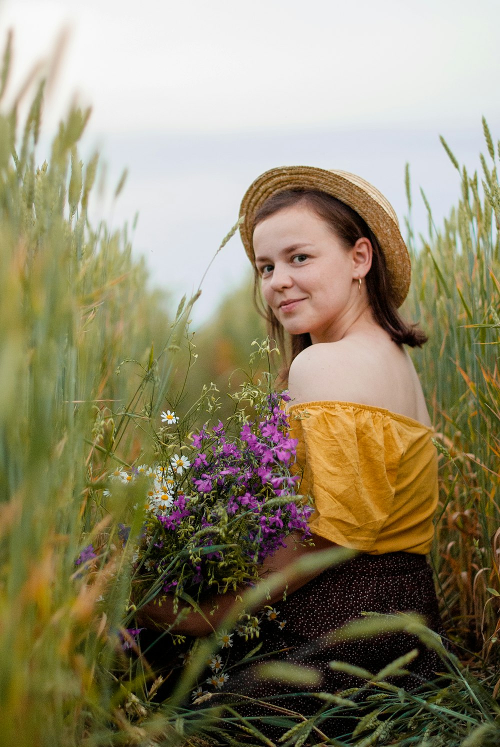 woman in yellow off shoulder shirt holding purple flowers