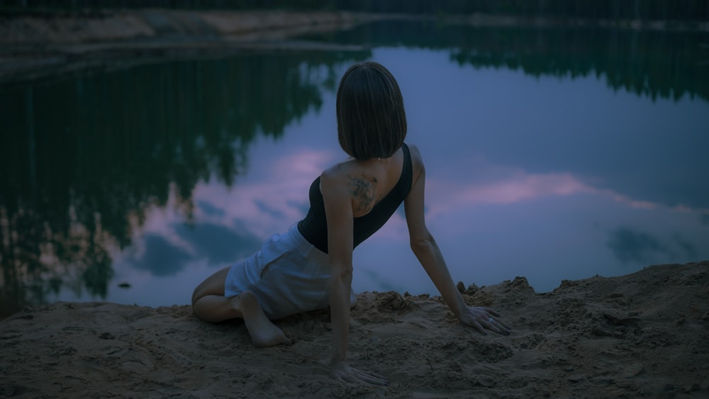 woman in black tank top and white shorts sitting on brown rock near body of water