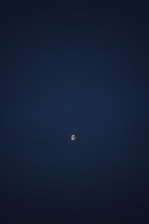 A celestial body resembling the moon is visible against a dark sky, partially obscured by clouds. The overall scene is dimly lit with a small spotlight effect on the moon-like object.