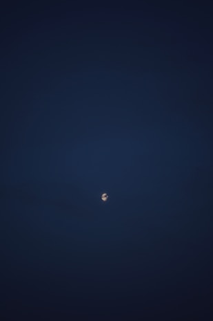 A celestial body resembling the moon is visible against a dark sky, partially obscured by clouds. The overall scene is dimly lit with a small spotlight effect on the moon-like object.