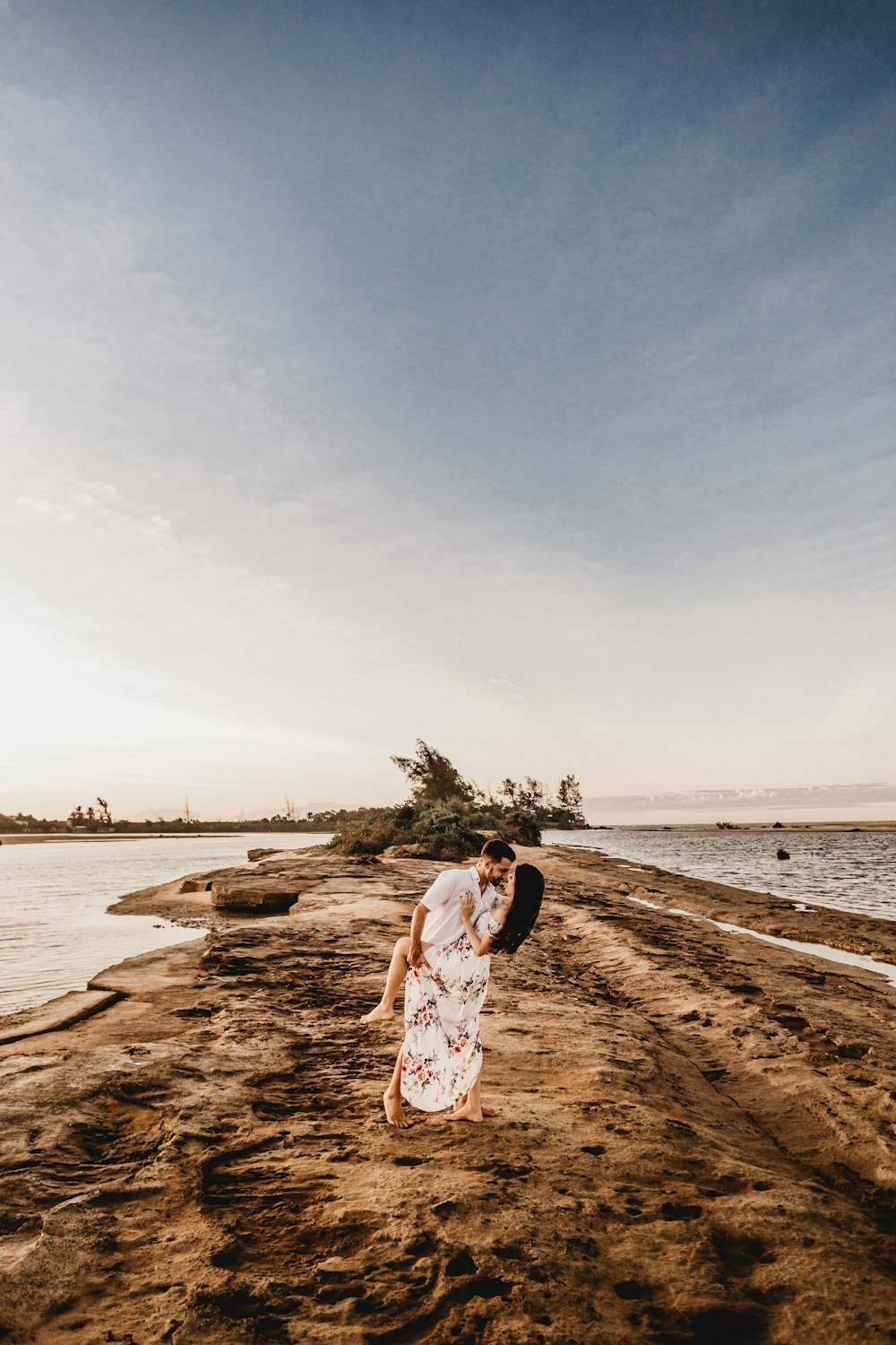 woman in white and brown dress standing on brown sand near body of water during daytime