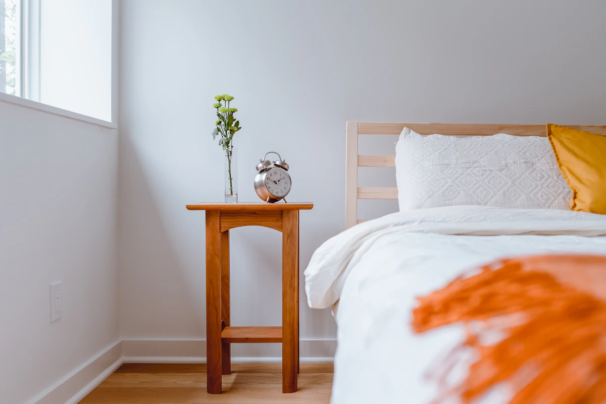 A small wooden bedside table next to a bed