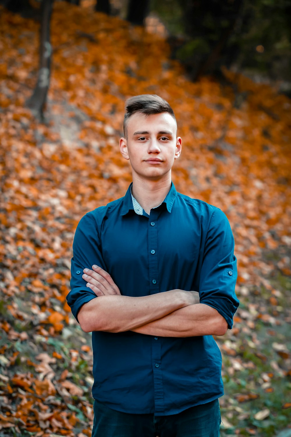 man in blue dress shirt standing on brown dried leaves during daytime