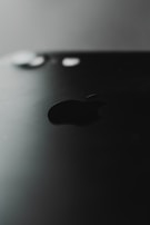 A close-up view of a black smartphone featuring the prominent logo of a well-known tech company. The back of the phone is shown, highlighting its sleek design with a matte finish. The camera lens and flash are visible at the top.