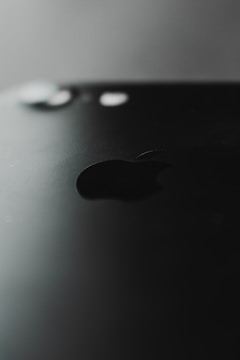 A close-up view of a black smartphone featuring the prominent logo of a well-known tech company. The back of the phone is shown, highlighting its sleek design with a matte finish. The camera lens and flash are visible at the top.