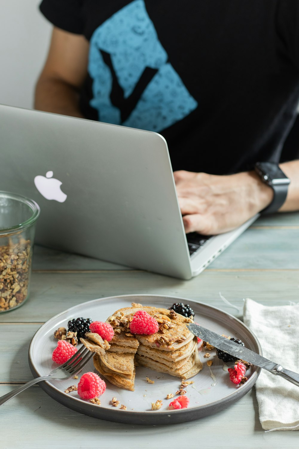 person holding silver macbook near cookies on white ceramic plate