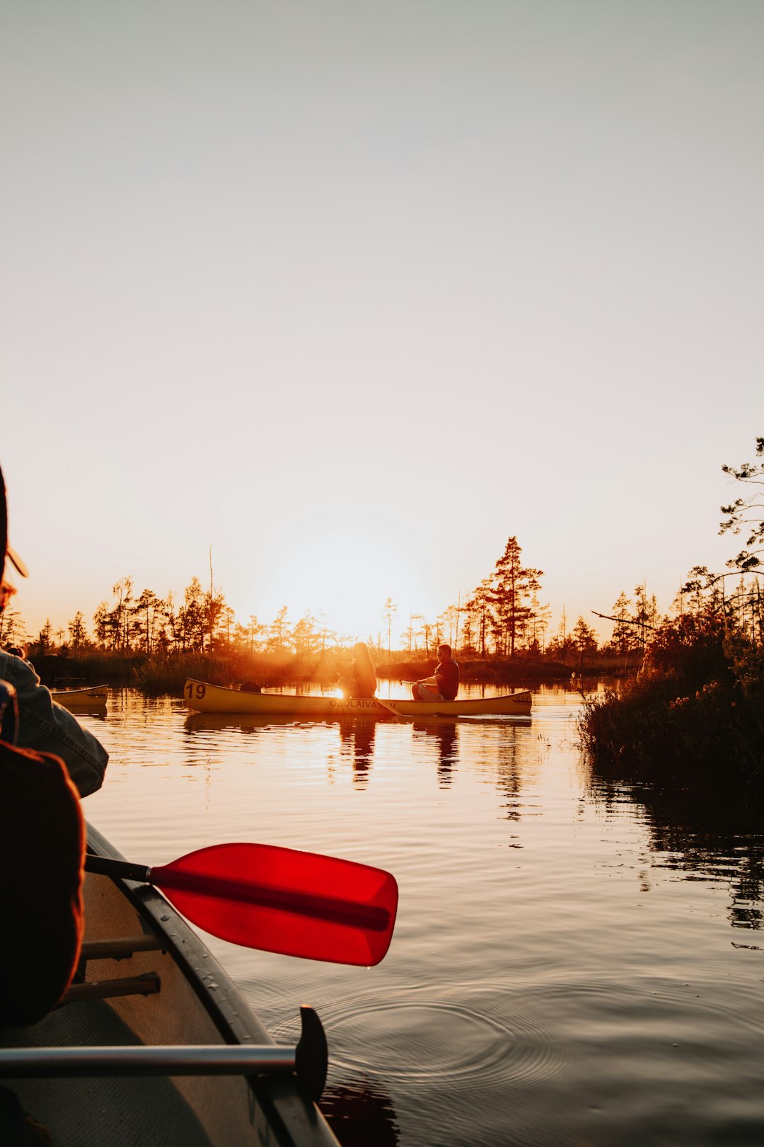 man in black hoodie sitting on red kayak during sunset