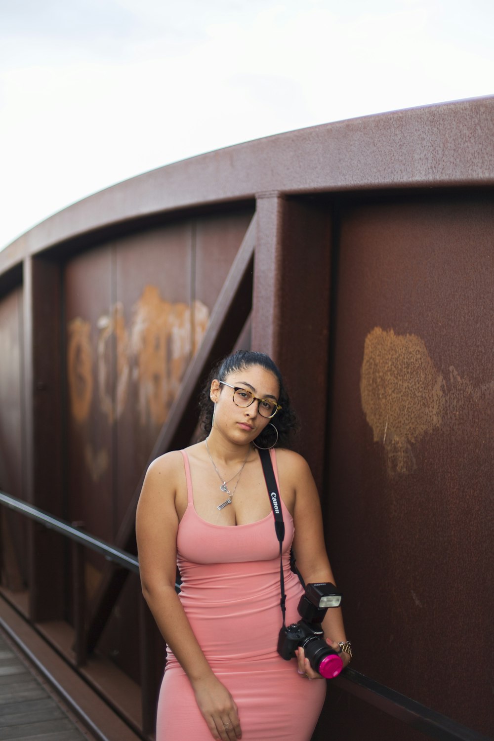woman in pink tank top wearing black sunglasses standing beside brown wooden wall during daytime