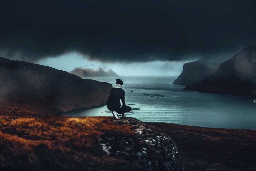 man in black shirt and pants standing on rock formation near body of water during daytime