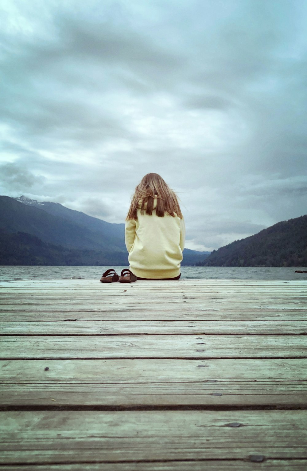 woman in beige long sleeve shirt sitting on brown wooden dock during daytime