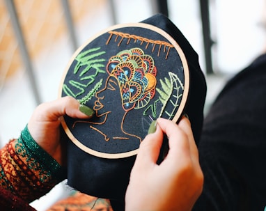Person holding a embroidered piece of fabric displaying a woman with a headpiece.