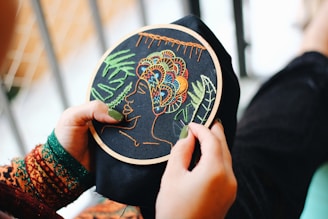 Person holding a embroidered piece of fabric displaying a woman with a headpiece.