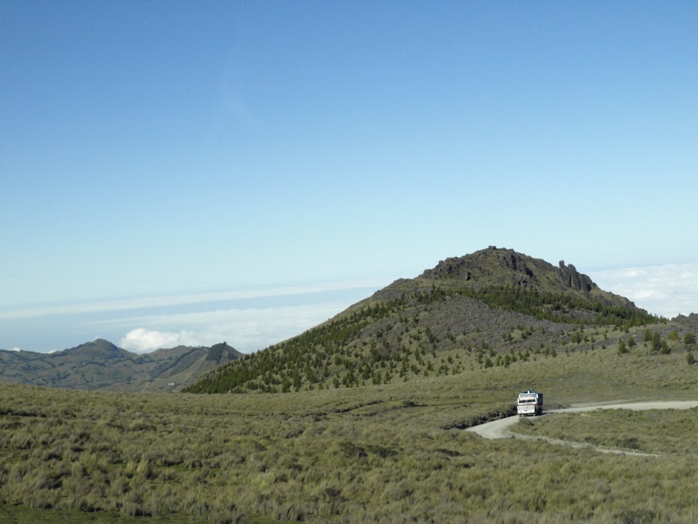 Furgoneta blanca en la carretera cerca de la montaña verde bajo el cielo azul durante el día