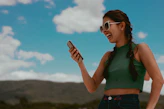 woman in green tank top holding smartphone during daytime