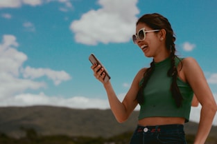 woman in green tank top holding smartphone during daytime