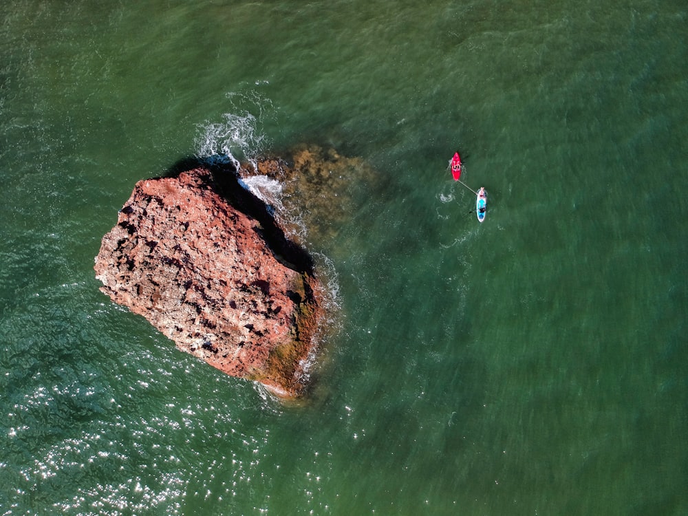 person in blue shirt and blue shorts standing on brown rock in the middle of water