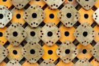 A repeating pattern of rusted metal plates with circular holes in the center and along their edges. The plates are stacked in a coordinated manner, alternating between metal and painted yellow surfaces, creating a geometric and industrial appearance.