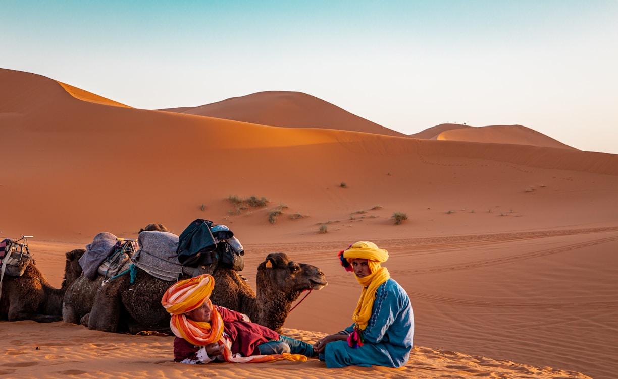 man in yellow robe sitting on brown sand during daytime