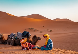 man in yellow robe sitting on brown sand during daytime