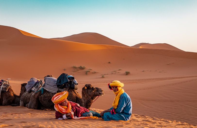 man in yellow robe sitting on brown sand during daytime