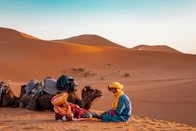 man in yellow robe sitting on brown sand during daytime