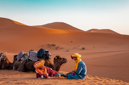 man in yellow robe sitting on brown sand during daytime