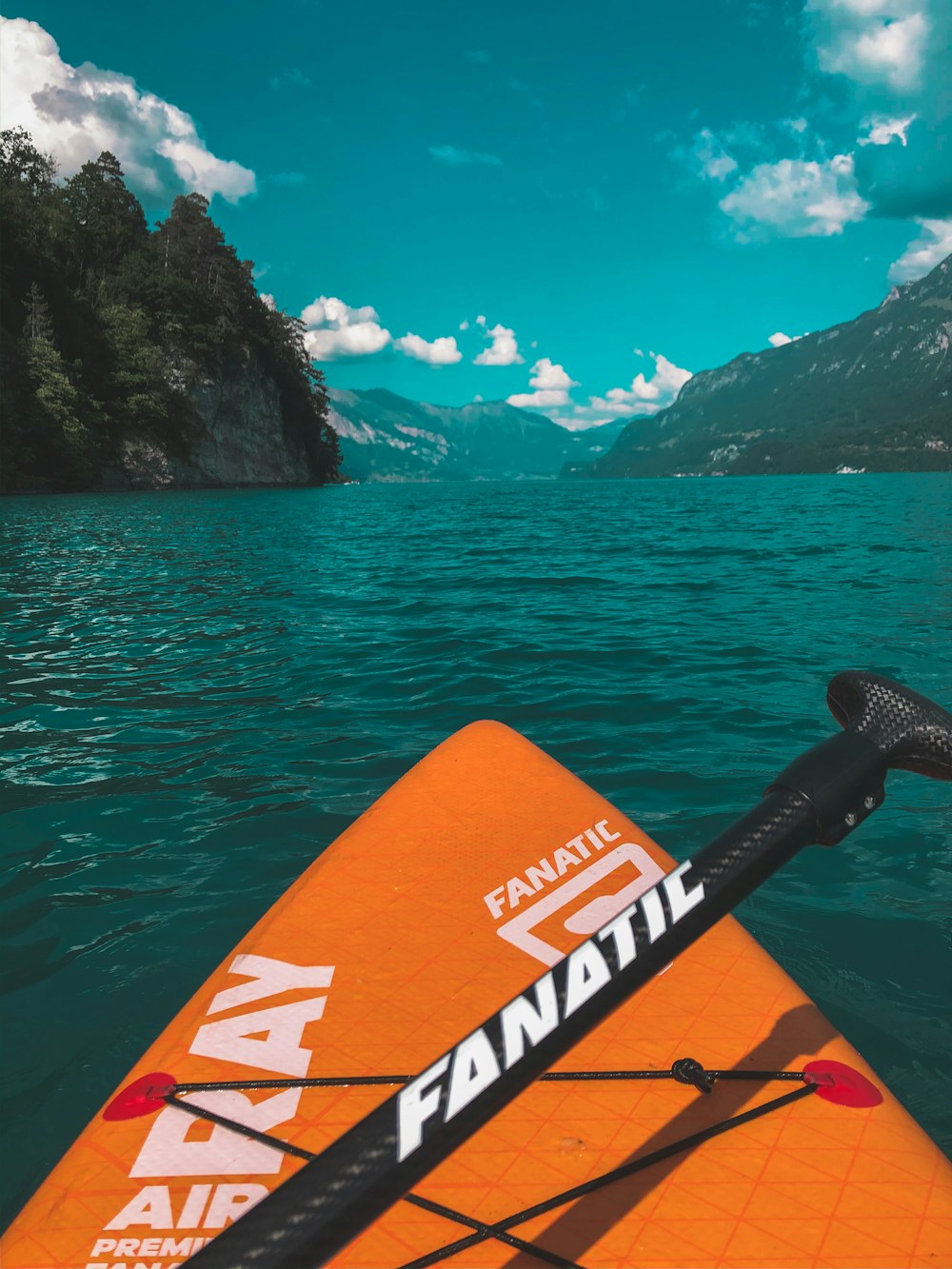 orange and black kayak on water near green trees and mountain during daytime