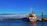 A sleek cargo ship docked at a busy port under a clear blue sky.