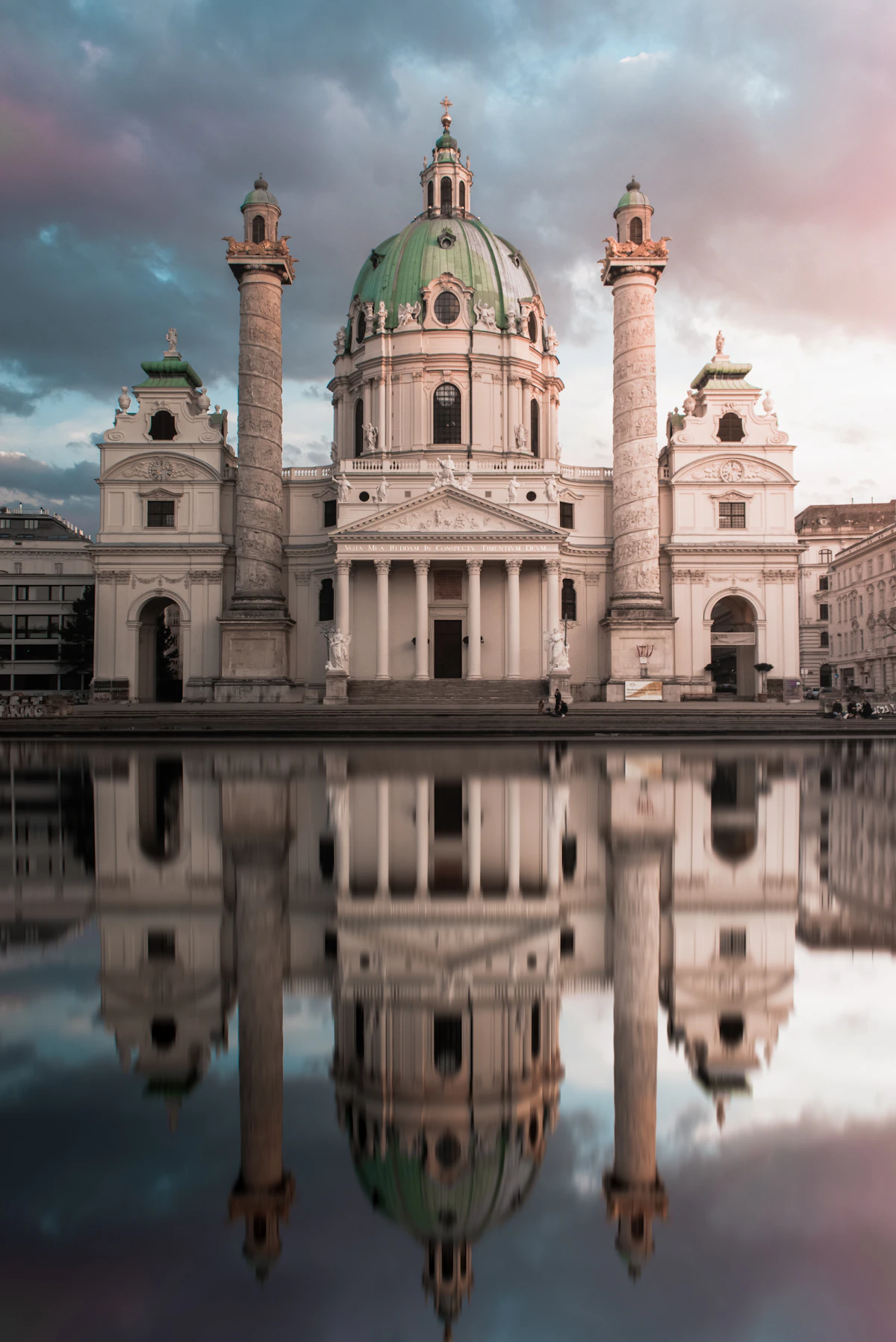 Karlskirche in Vienna reflected in a calm pool beneath a dramatic evening sky